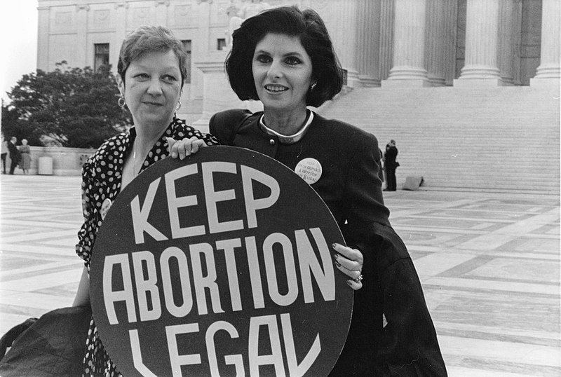 Norma McCorvey, left, who was Jane Roe in the 1973 Roe v. Wade case, with her attorney, Gloria Allred, outside the Supreme Court in April 1989, where the Court heard arguments in a case that could have overturned the Roe v. Wade decision. Image via. Wikimedia Commons