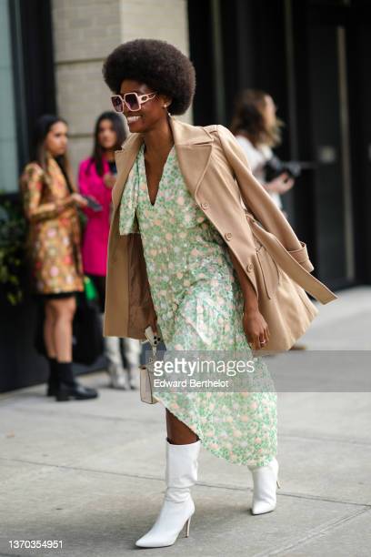 NEW YORK, NEW YORK - FEBRUARY 12: A guest wears pale pink sunglasses from D, a beige long belted coat, a beige and green embroidered sequins flower pattern ruffled V-neck / asymmetric midi dress, a beige matte leather handbag, white leather pointed heels knees boots, a silver and diamond ring, outside Song Jun Wan, during New York Fashion Week, on February 12, 2022 in New York City. (Photo by Edward Berthelot/Getty Images)