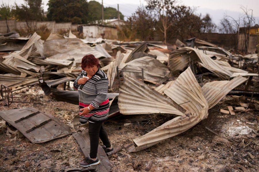 Rosa Munoz walks among the debris of her home destroyed by wildfires, in Tome, Chile, Saturday, Feb. 4, 2023. Forest fires are spreading in southern and central Chile, triggering evacuations and the declaration of a state of emergency in some regions. (AP Photo/Matias Delacroix)